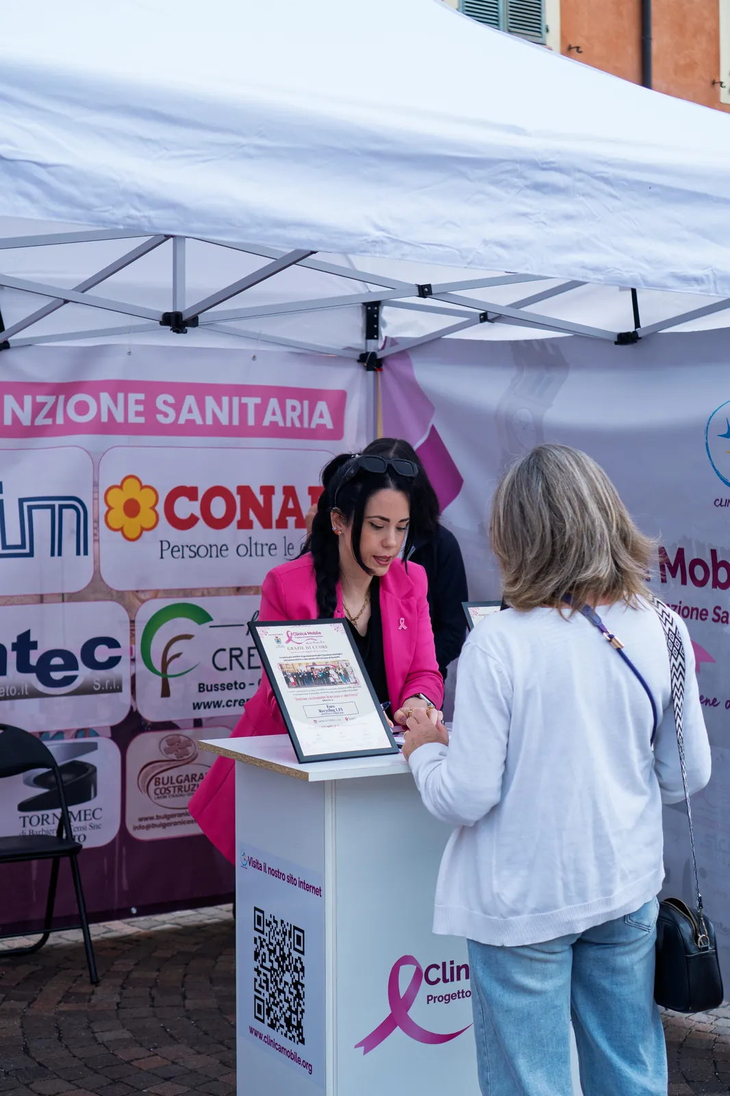 Un'operatrice in giacca rosa registra una signora al banco della prevenzione a Busseto