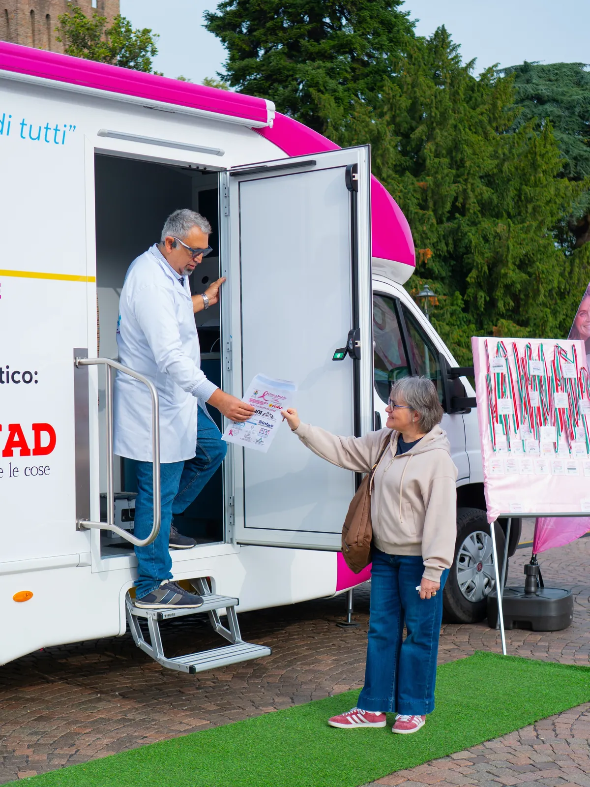 Il medico consegna un foglio a una signora sulla porta dell'ambulatorio mobile a Busseto