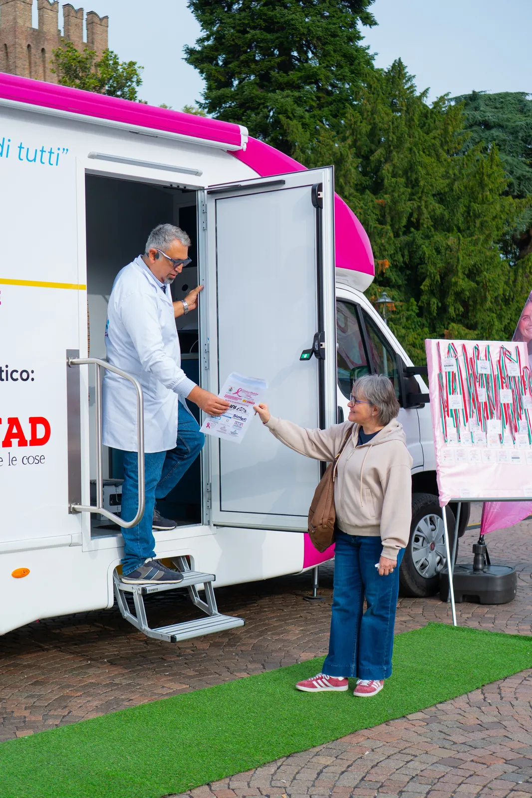 Il medico consegna un foglio a una signora sulla porta dell'ambulatorio mobile a Busseto