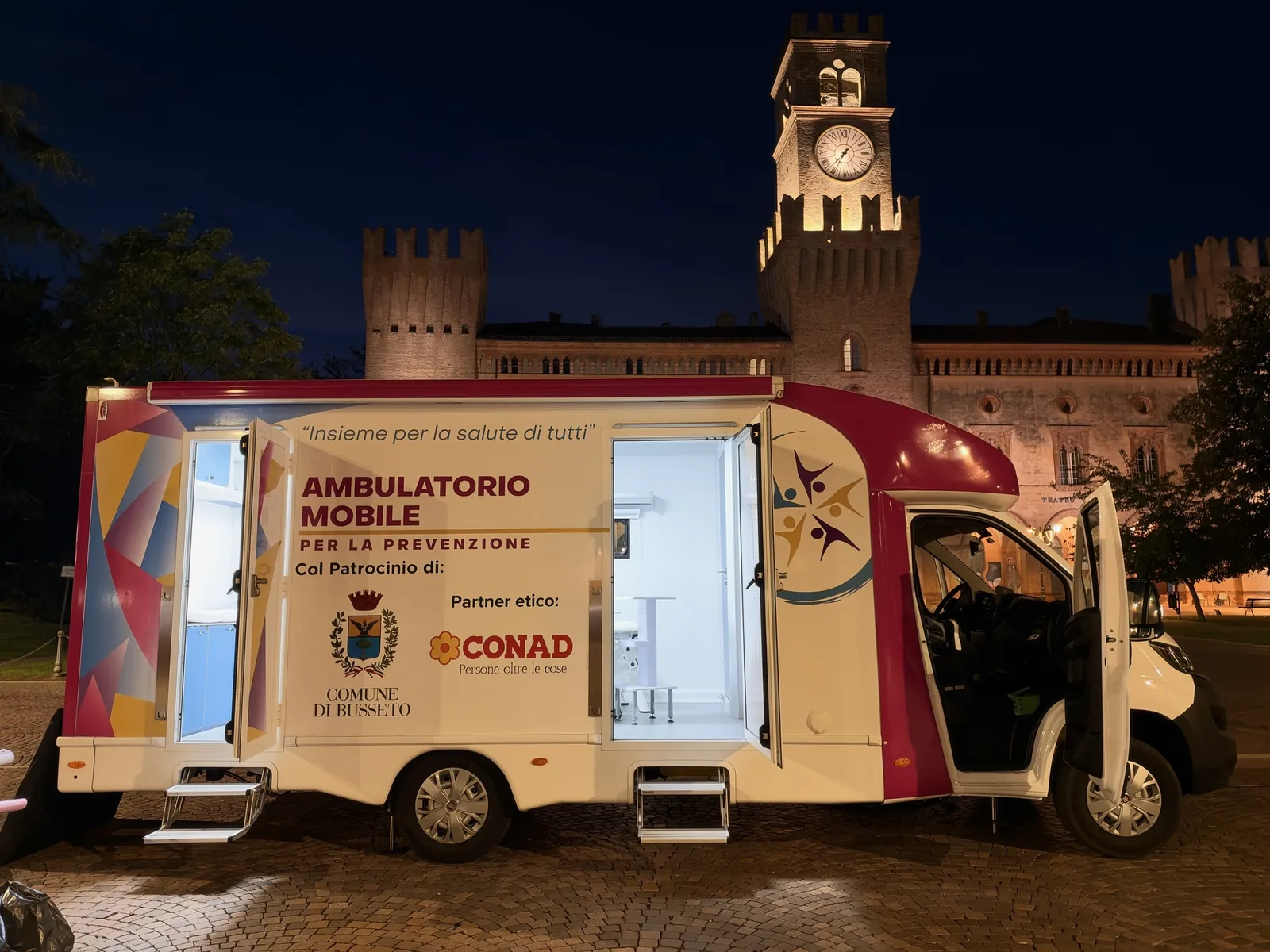 L'ambulatorio mobile di sera sotto la torre dell'orologio illuminata di Busseto