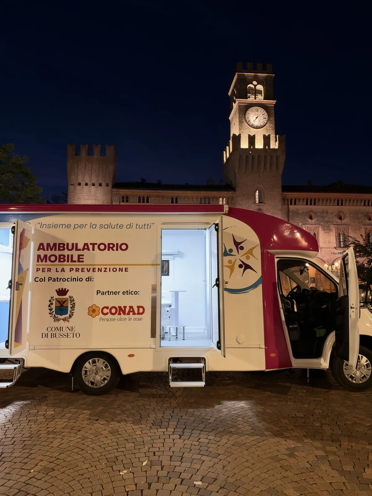 La torre dell'orologio di Busseto illuminata sopra l'ambulatorio mobile