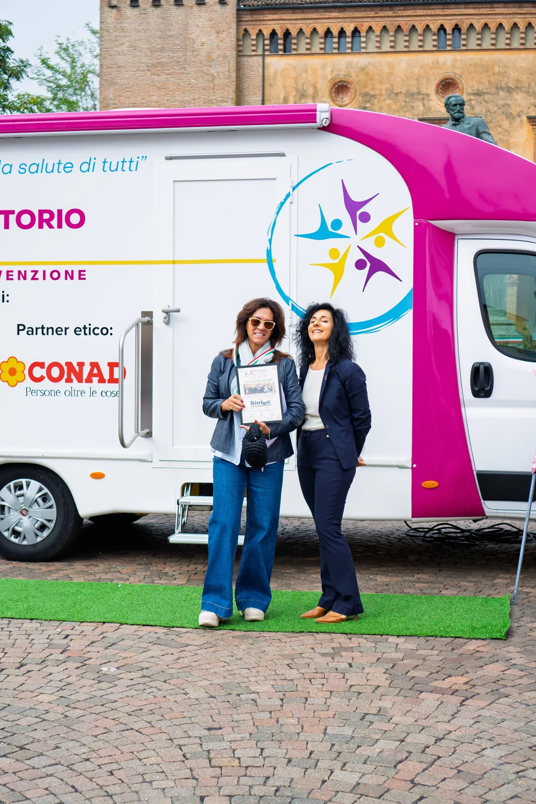 Due donne sorridenti con l'attestato davanti all'ambulatorio mobile