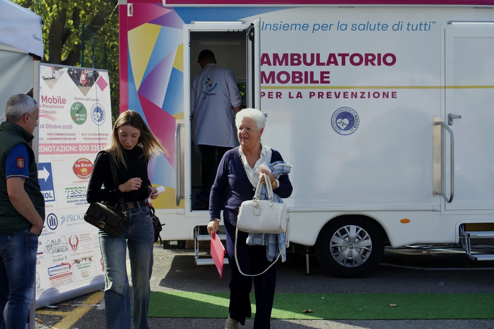 Una signora sorridente con la cartellina rosa si allontana dall'ambulatorio mobile