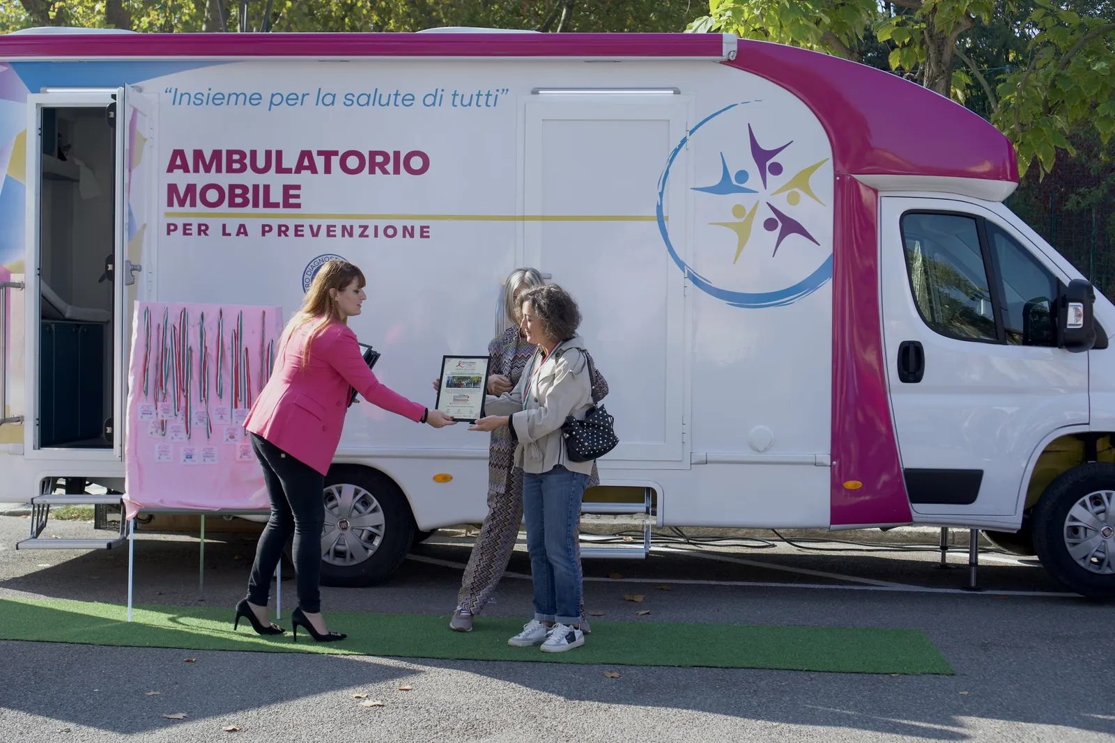 Un'operatrice consegna un attestato davanti all'ambulatorio mobile a Castell'Arquato