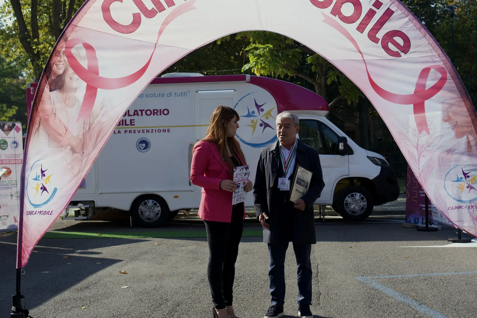 Consegna di un attestato sotto l'arco rosa di Clinica Mobile