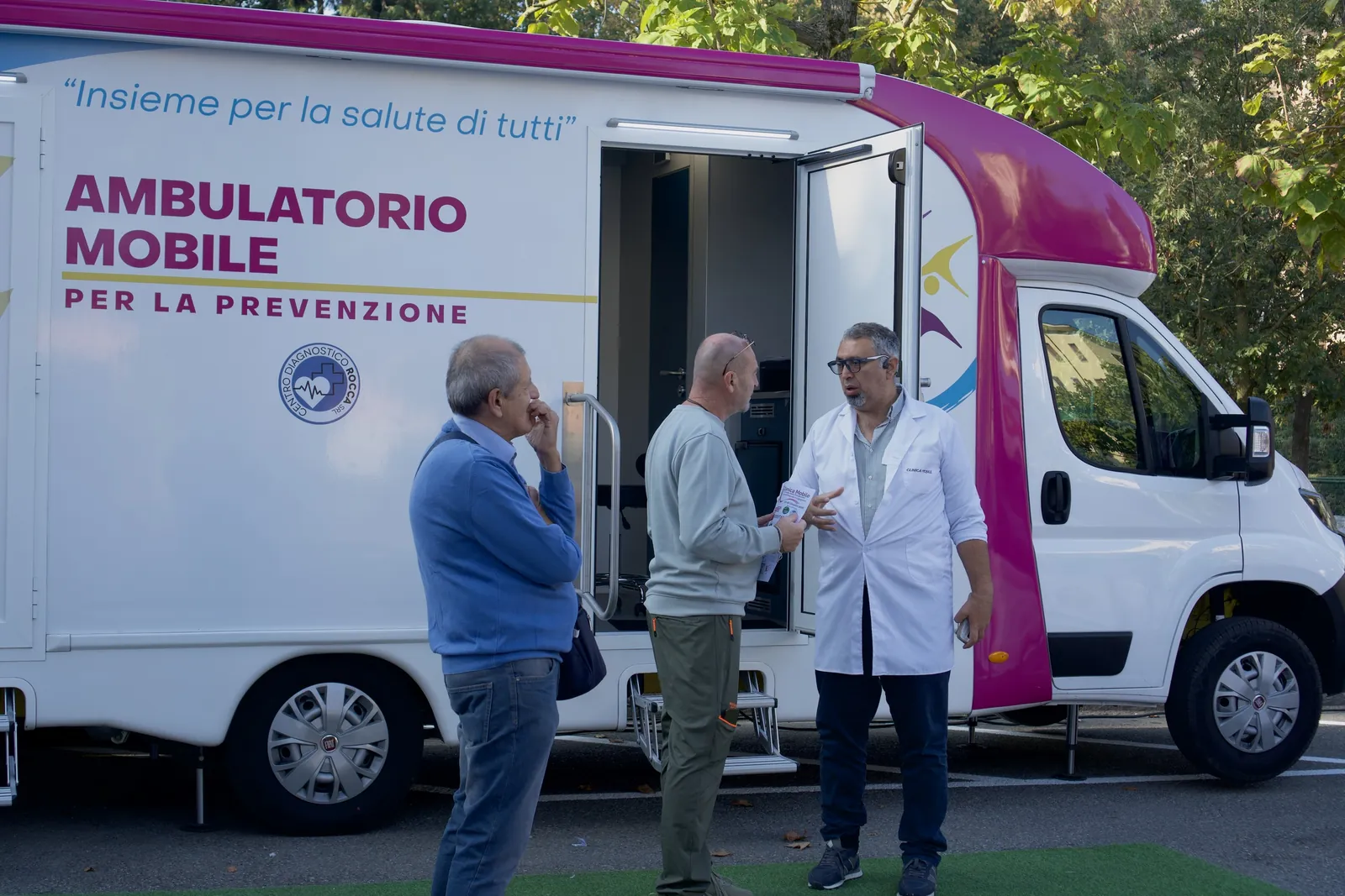 Il medico in camice parla con due signori davanti all'ambulatorio mobile a Castell'Arquato