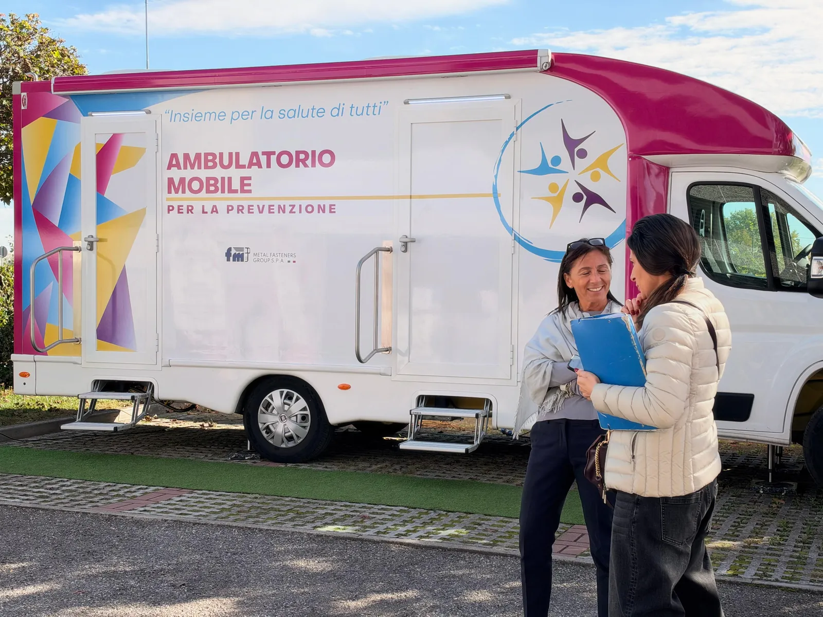 Due dipendenti di FM con la cartellina davanti all'ambulatorio mobile