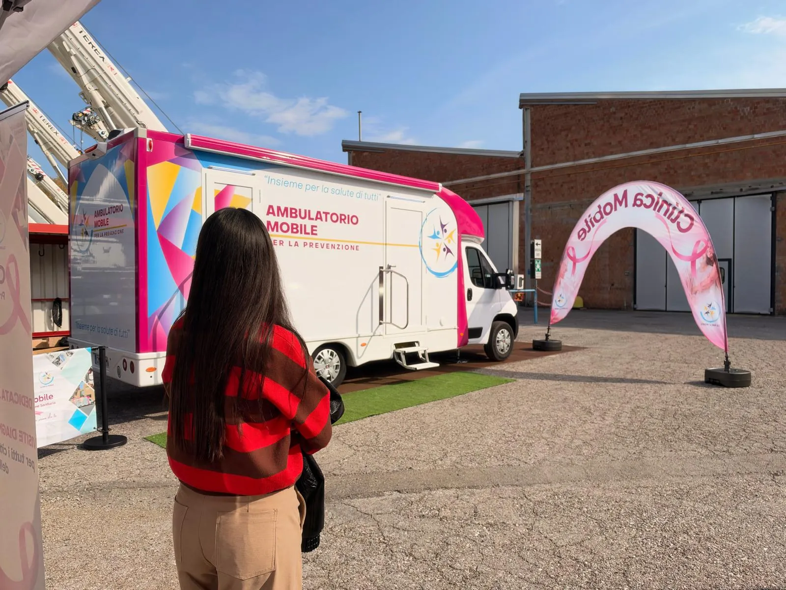 Una dipendente di RT Cranes davanti all'ambulatorio mobile e all'arco rosa nel piazzale dell'azienda a Crespellano