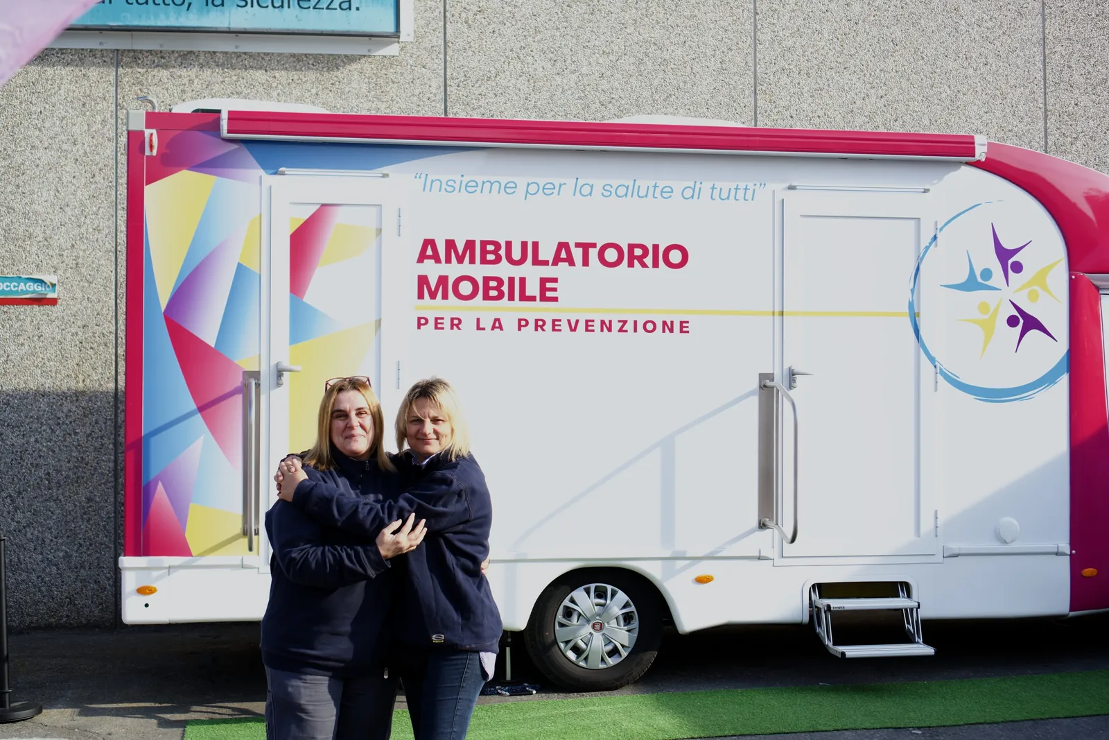 Due colleghe si abbracciano davanti all'ambulatorio mobile di Clinica Mobile in Wittur